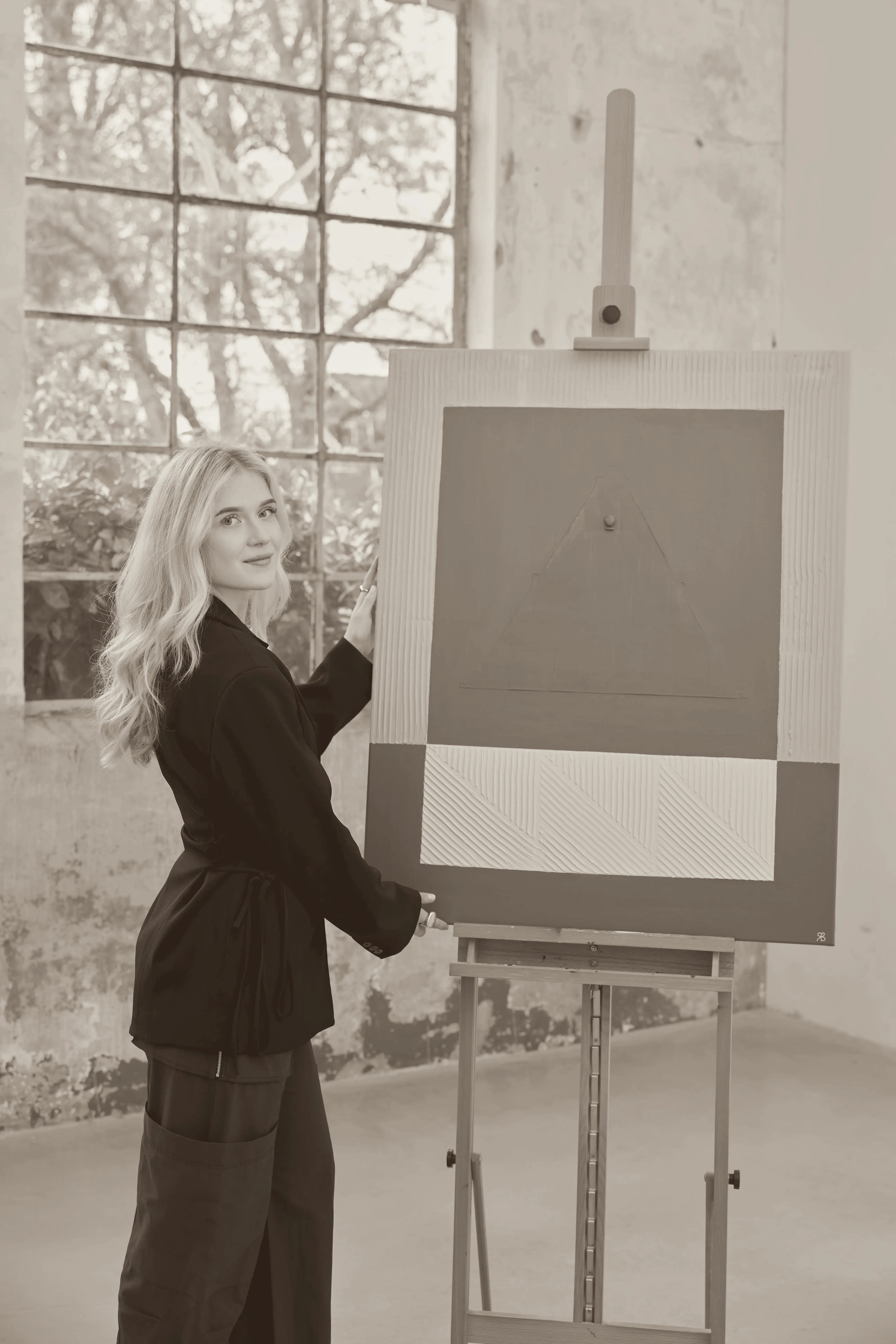 Robin Blankendaal in haar atelier, met een hand op een ezel met een doek